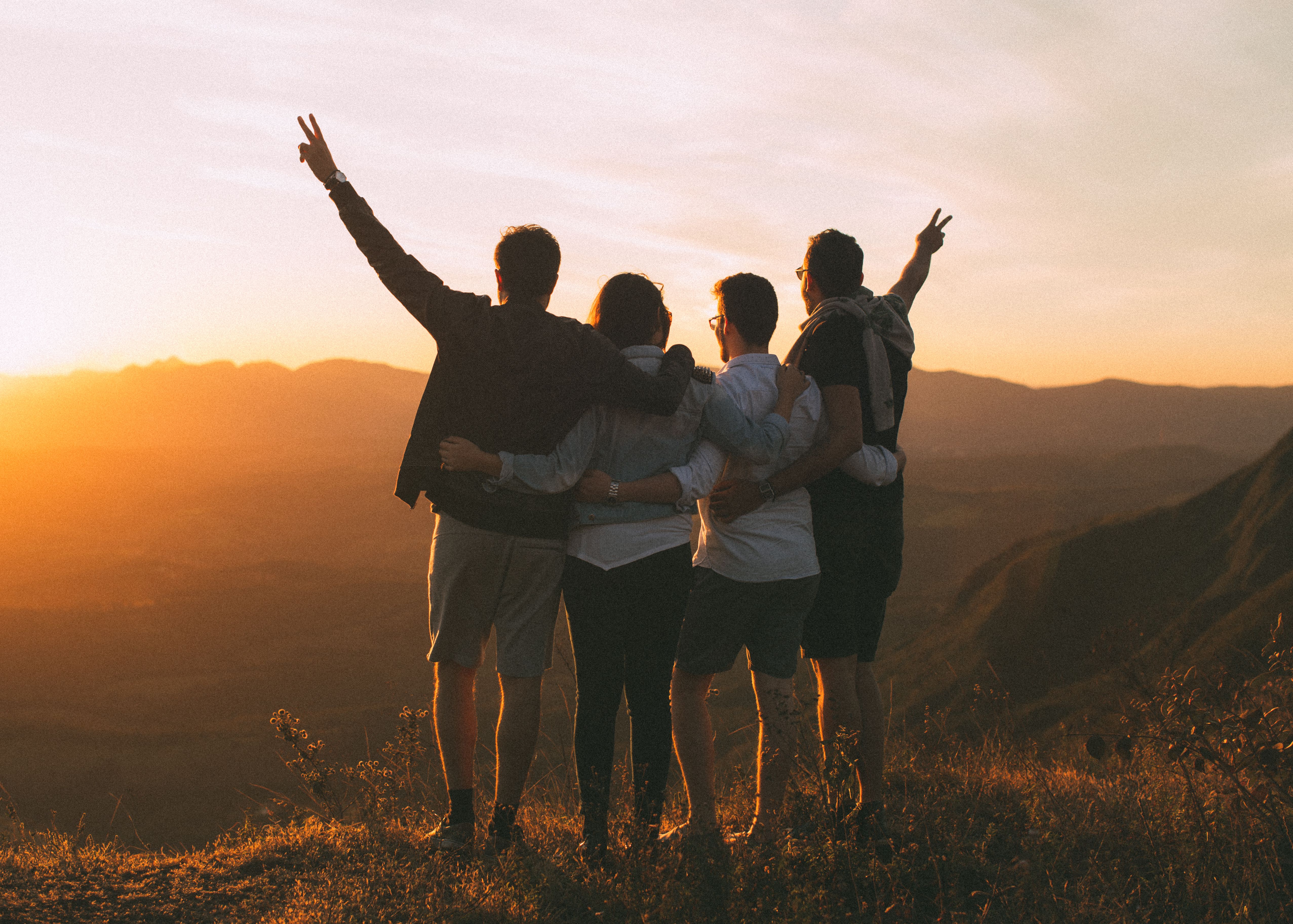 Five friends embracing as they watch a golden sunset from a mountain overlook